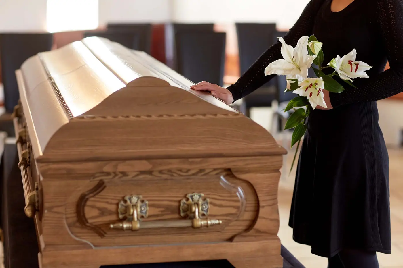 People and mourning concept - woman with white lily flowers and coffin at funeral in church